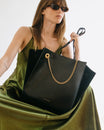 Sac cabas LEXI GM noir porté à la main, détail de la chaîne amovible dorée, sur robe verte