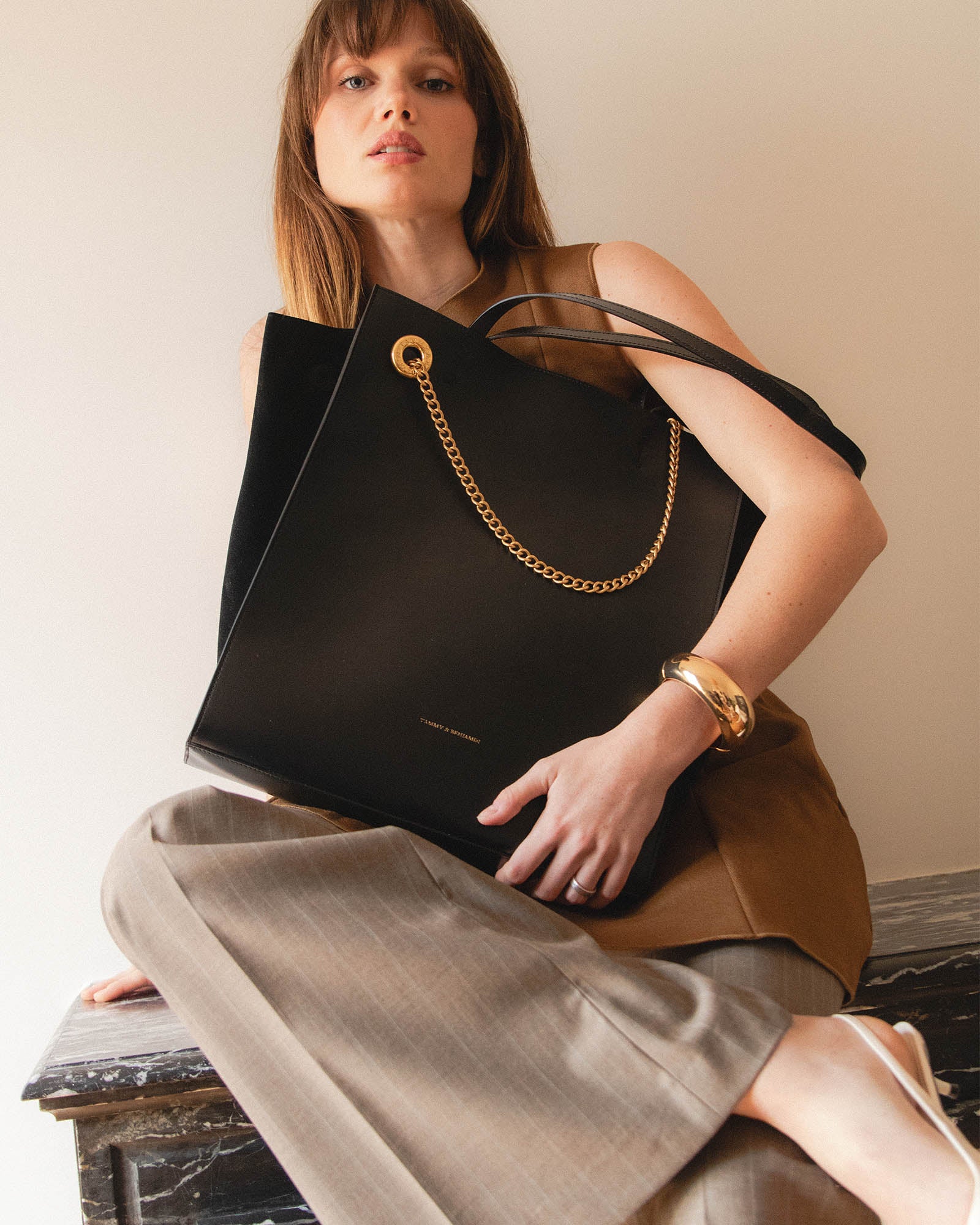 LEXI GM Noir, porté sous le bras par une femme assise, chaîne dorée amovible visible