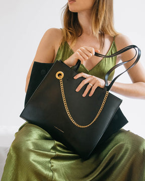 Cabas LEXI MM noir, tenu à la main et posé sur les genoux, détail de la chaîne dorée amovible
