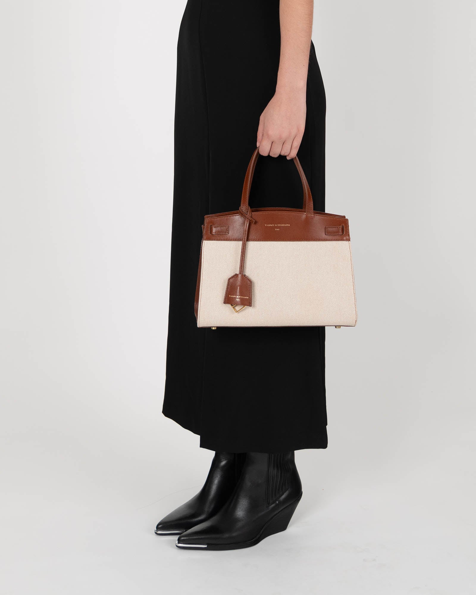 MADISON bag in brown and canvas held by hand, front view showing short handles and leather luggage tag