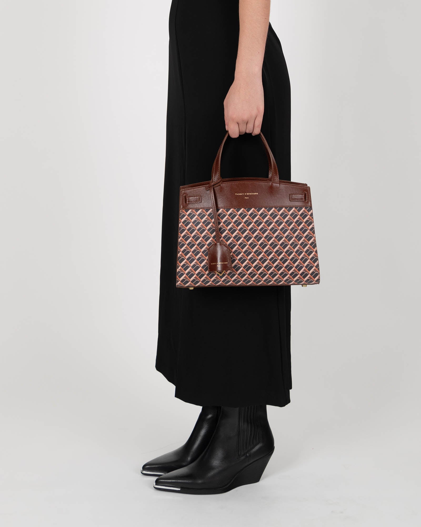 MADISON bag in brown monogram held by hand by a woman in a black dress, side view