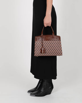 MADISON bag in brown monogram held by hand by a woman in a black dress, side view