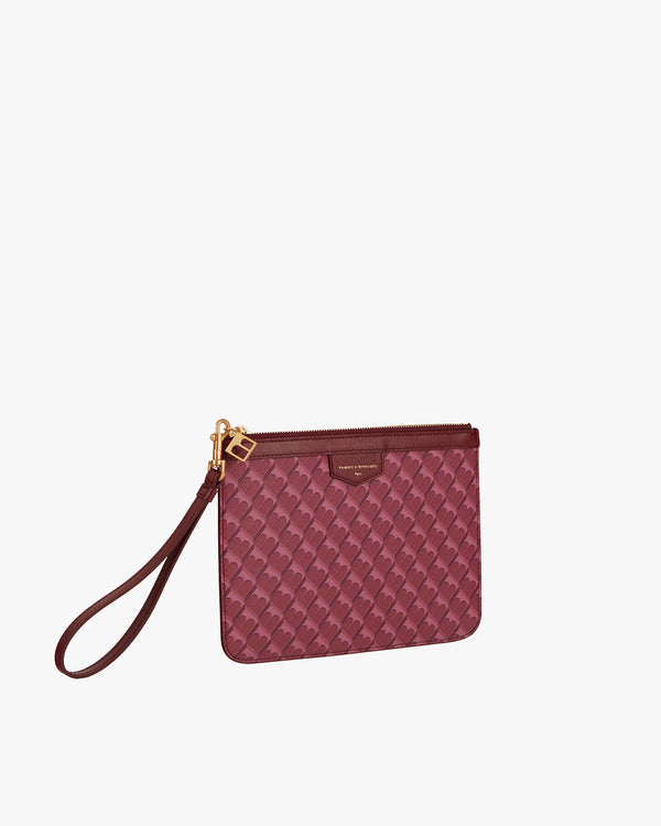 Pochette PM Monogram Bordeaux, vue de trois quarts avec dragonne en cuir posée au sol