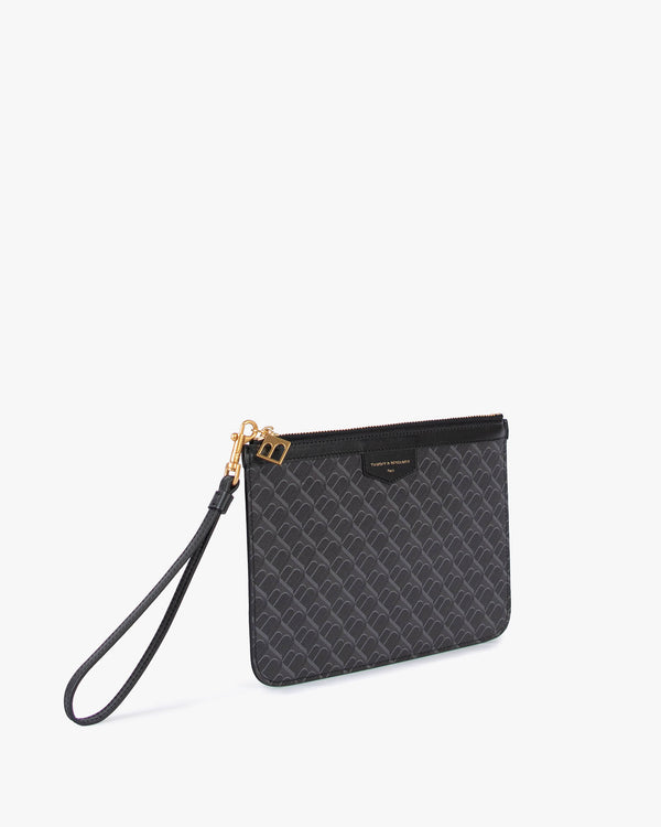 Pochette PM Monogram noire de trois quarts, dragonne en cuir détachée posée devant