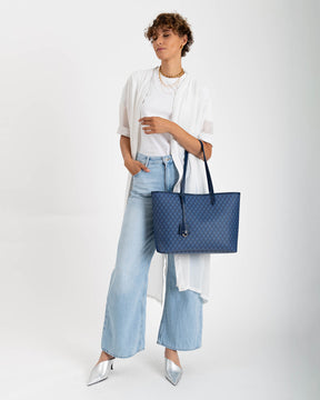 TOTE MONOGRAM bleu, porté à la main par une femme, en toile enduite à motif