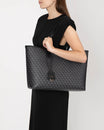 TOTE MONOGRAM noir, porté épaule par une femme, vue de profil, anses plates en cuir