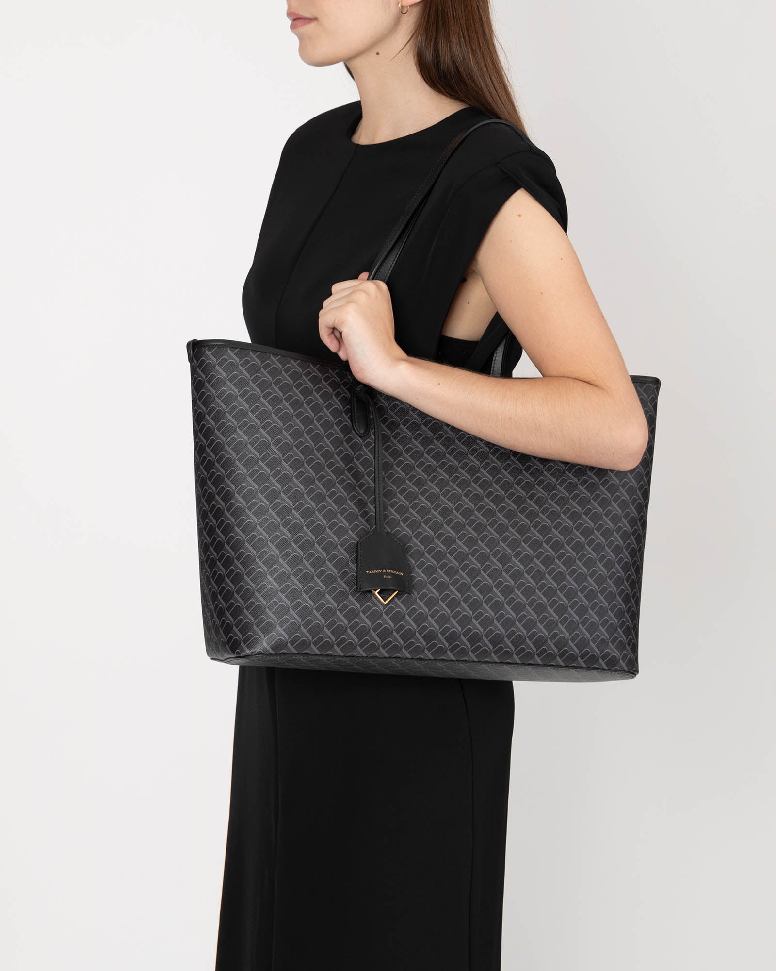 TOTE MONOGRAM noir, porté épaule par une femme, vue de profil, anses plates en cuir