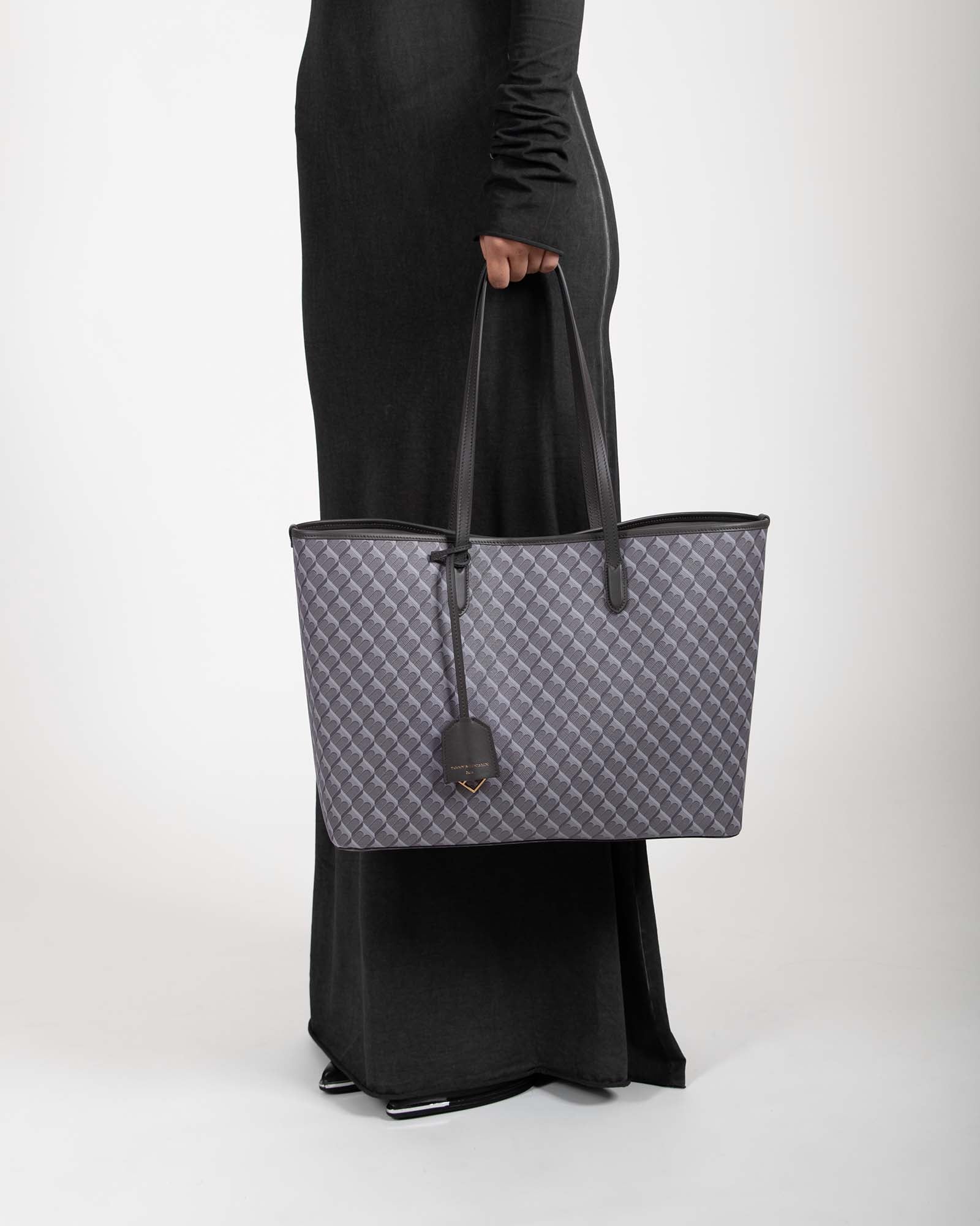 TOTE MONOGRAM gris porté à la main, vue de côté sur un modèle, anses en cuir
