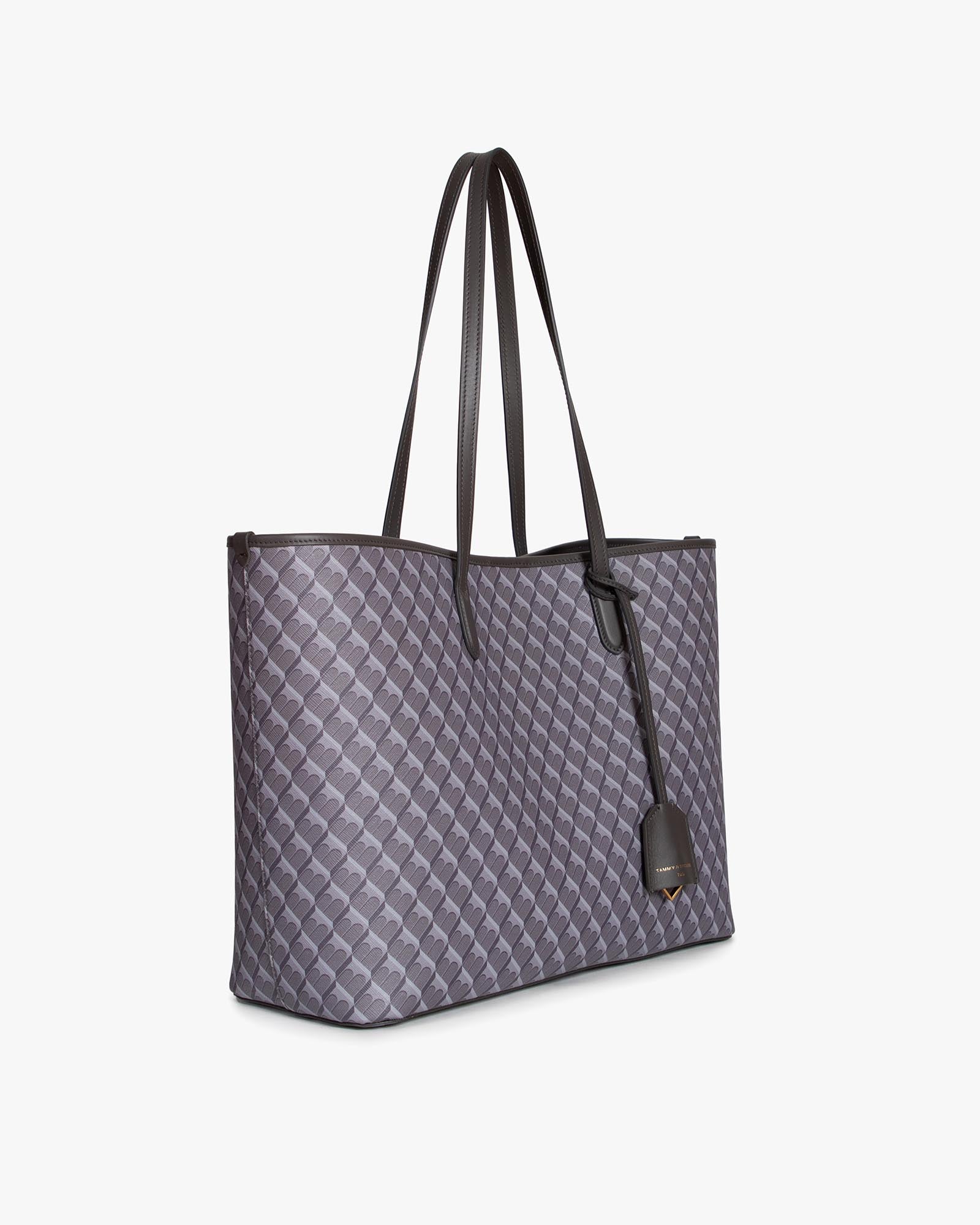 Sac TOTE MONOGRAM gris, vue de trois-quarts, posé, avec anses longues en cuir et étiquette pendante