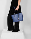 TOTE MONOGRAM PM bleu en toile enduite, porté à la main par une femme en robe noire
