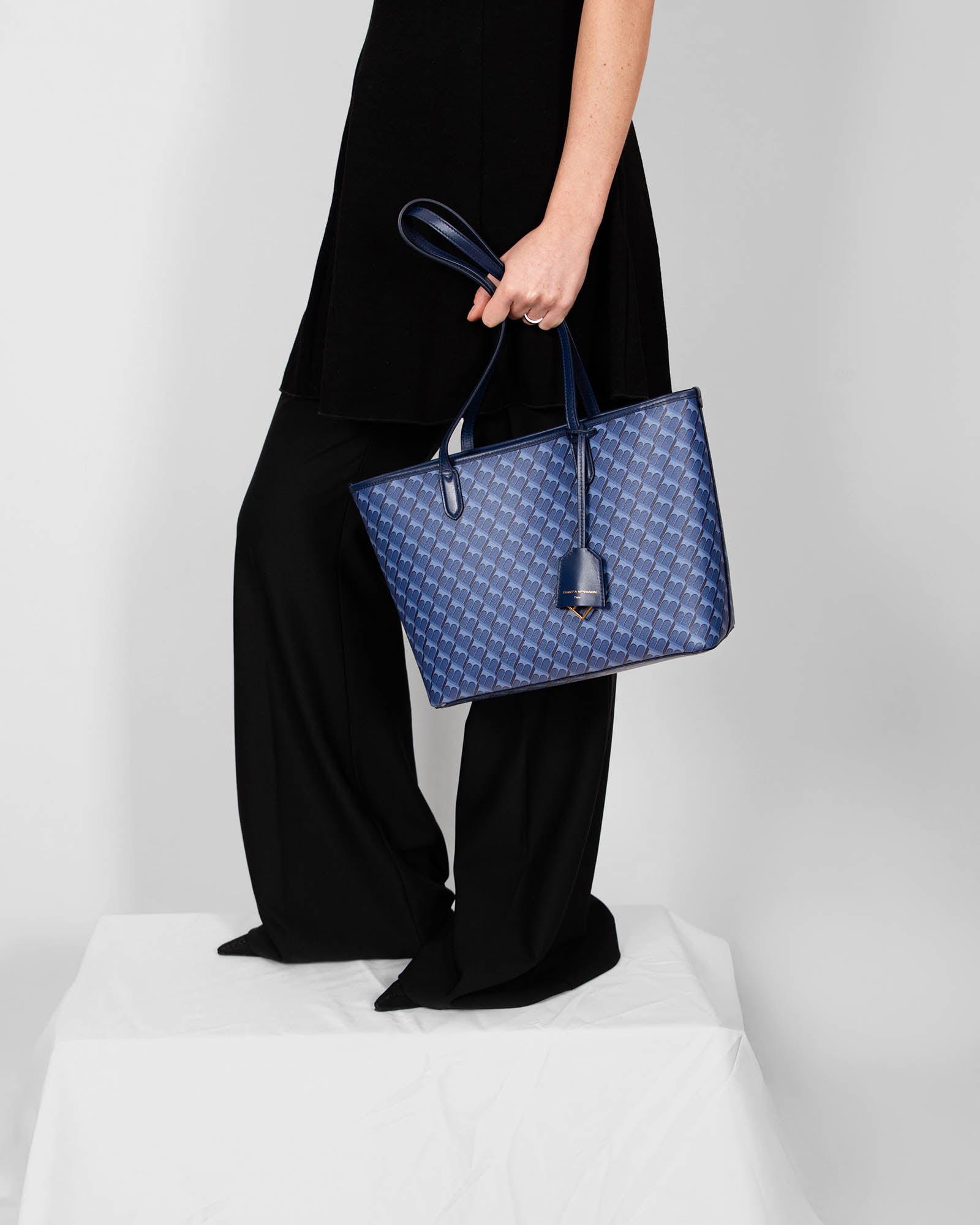 TOTE MONOGRAM PM bleu en toile enduite, porté à la main par une femme en robe noire