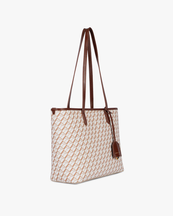 TOTE MONOGRAM PM Tan, vue de profil, porté à l'épaule par les deux anses en cuir, toile enduite à motif