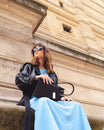 Sac TARA noir porté à la main, silhouette graphique, assise en extérieur devant un bâtiment