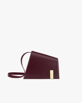 Sac TARA Mahogany de profil, fermoir plaque dorée, bandoulière fine détachée posée au sol