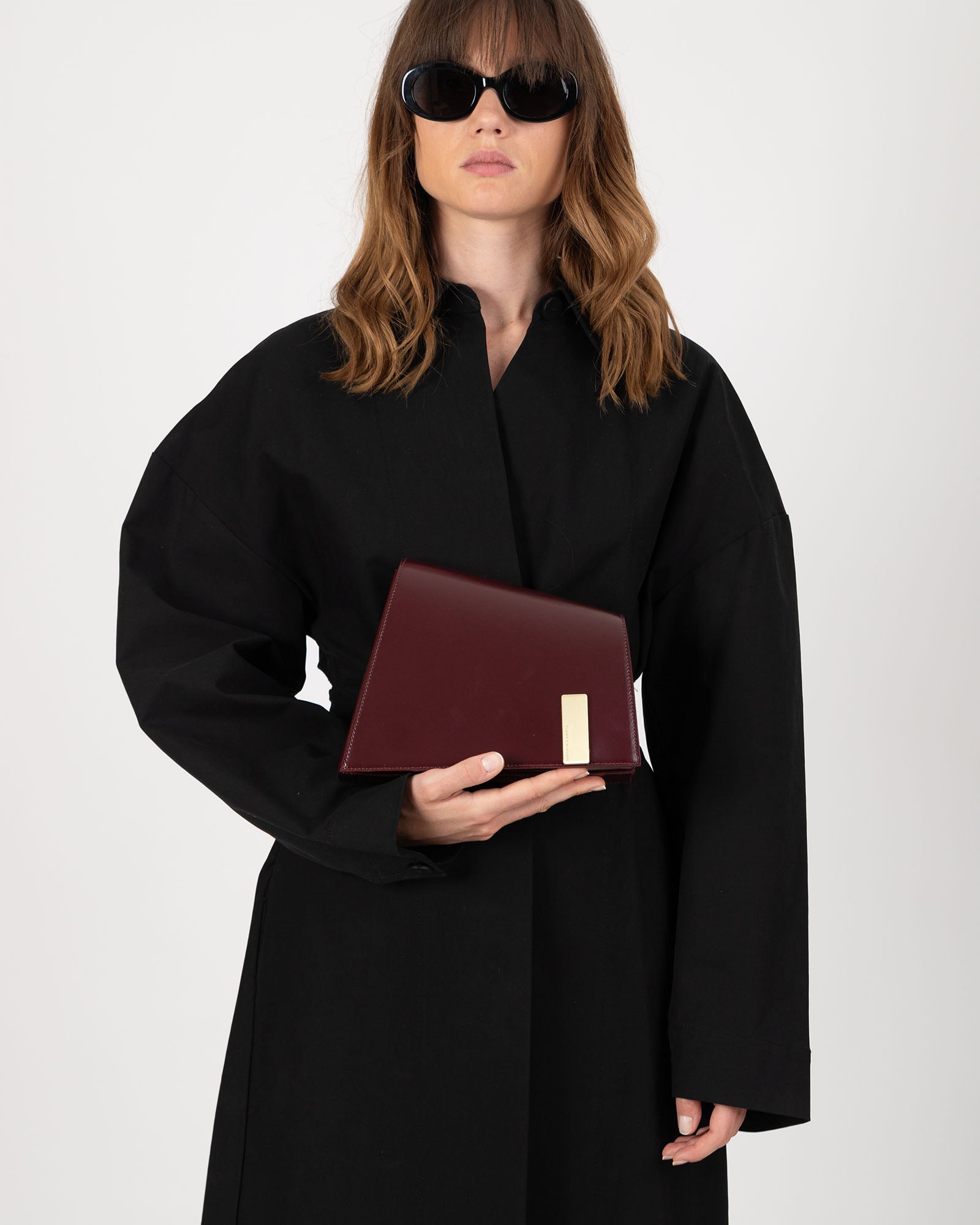 Sac TARA Mahogany tenu à la main, vue de face avec plaque logo dorée visible