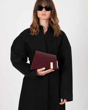 Sac TARA Mahogany tenu à la main, vue de face avec plaque logo dorée visible
