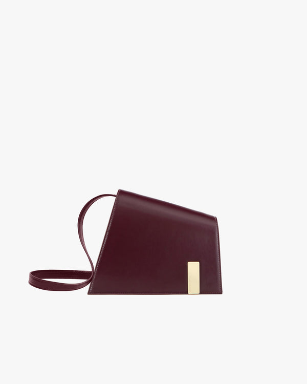 Sac TARA Mahogany de profil, fermoir plaque dorée, bandoulière fine détachée posée au sol
