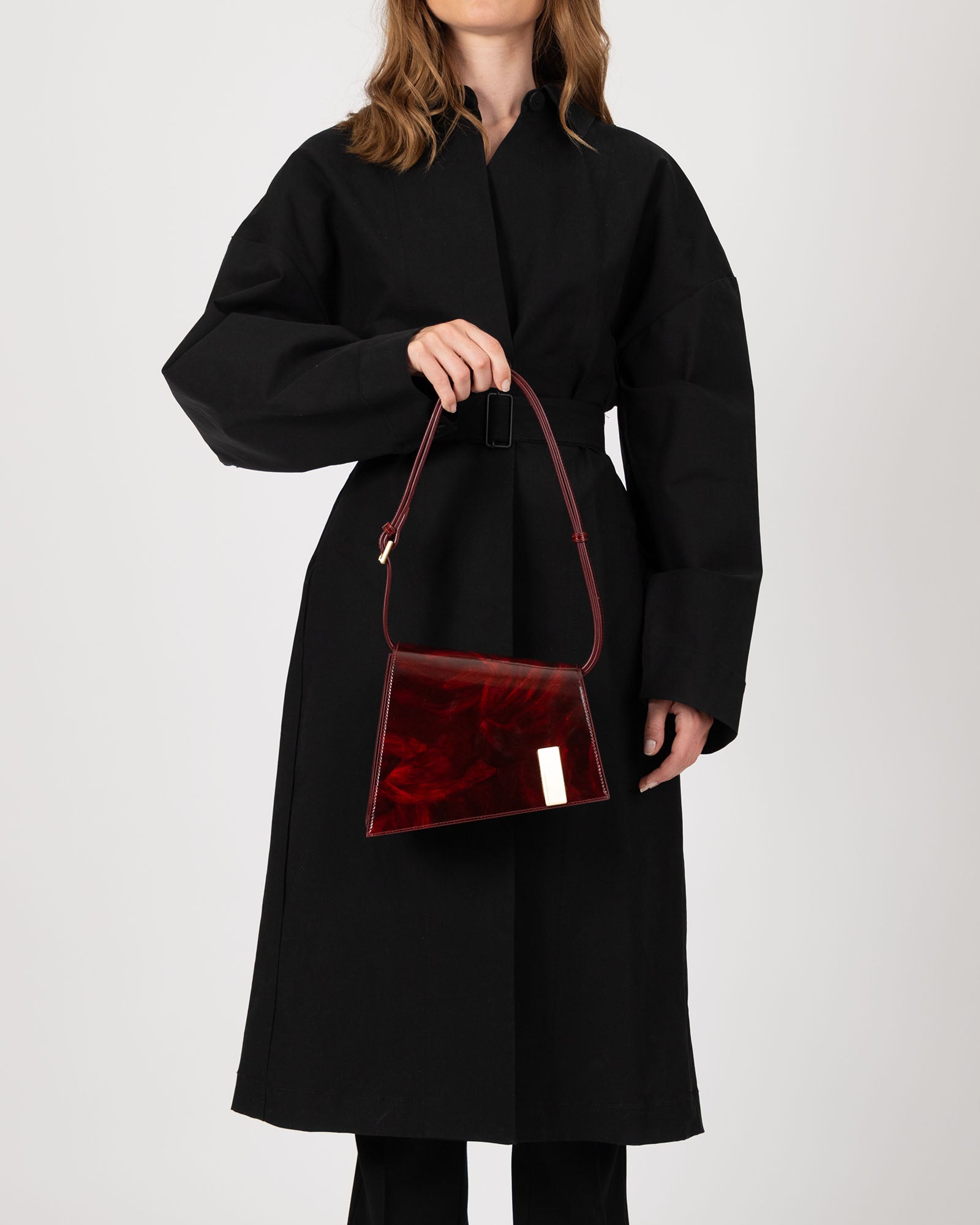 Sac TARA Marbre en cuir marbré, porté à la main par une femme en manteau noir, fermoir doré visible