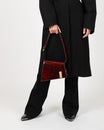 Sac TARA Marbre en cuir marbré rouge, porté à la main par un mannequin en tenue noire