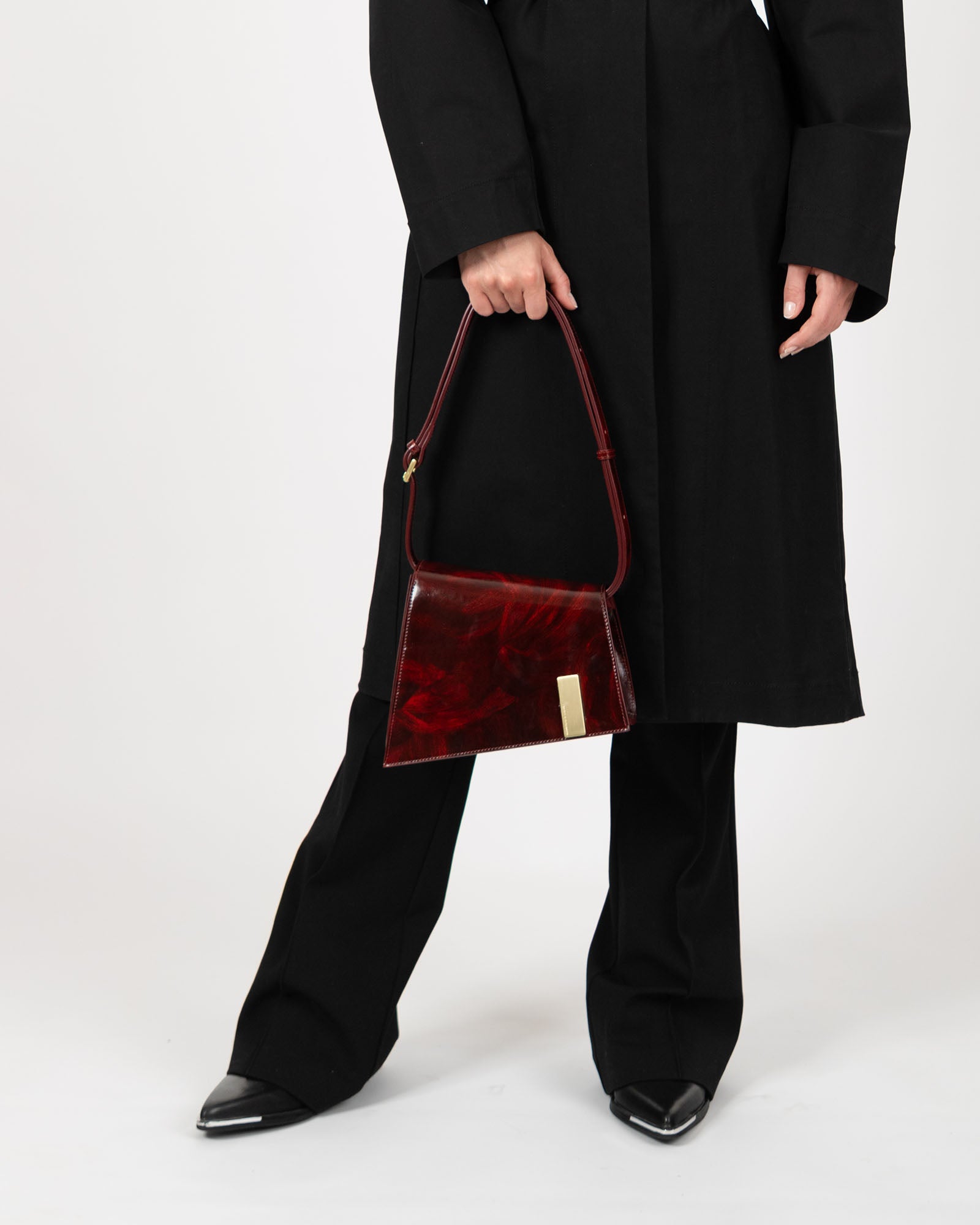 Sac TARA Marbre en cuir marbré rouge, porté à la main par un mannequin en tenue noire