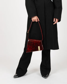 Sac TARA Marbre en cuir marbré rouge, porté à la main par un mannequin en tenue noire