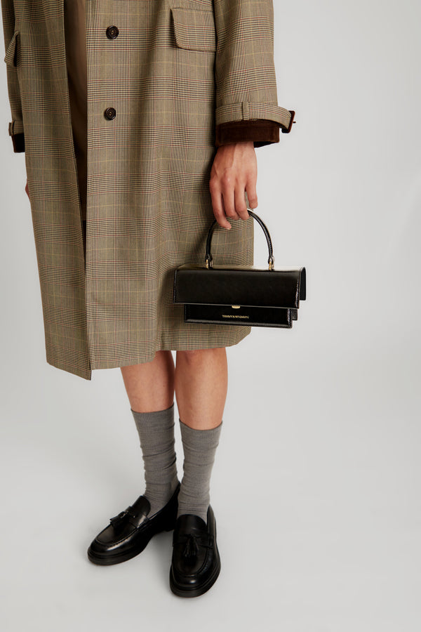 Sac THEA MINI noir naplak porté à la main, détail du fermoir, tenu par une personne en manteau prince de Galles