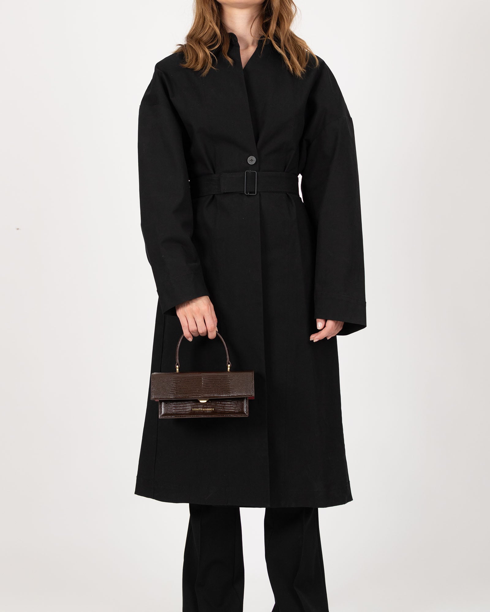 Sac THEA MINI brun embossé lézard, porté à la main par un mannequin en manteau noir