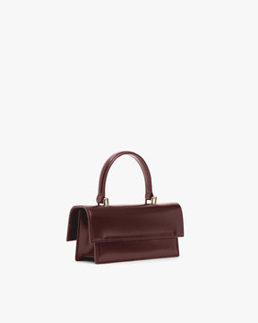THEA MINI bag in Mahogany, side view, placed down, flap closed with top handle raised
