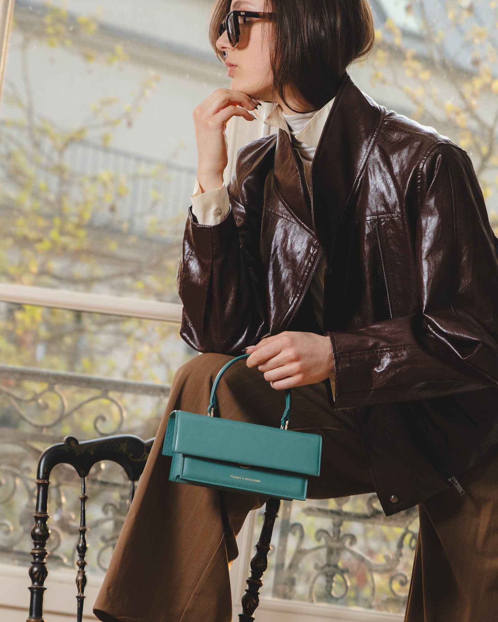 THEA MINI bag in turquoise, held by hand, side view on a seated woman