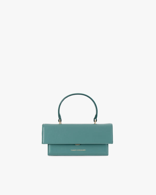Sac THEA MINI turquoise de face, posé, anse courte relevée, fermoir rabat visible