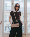 THEA beige bag worn crossbody, held by hand, rigid handle, gold clasp visible