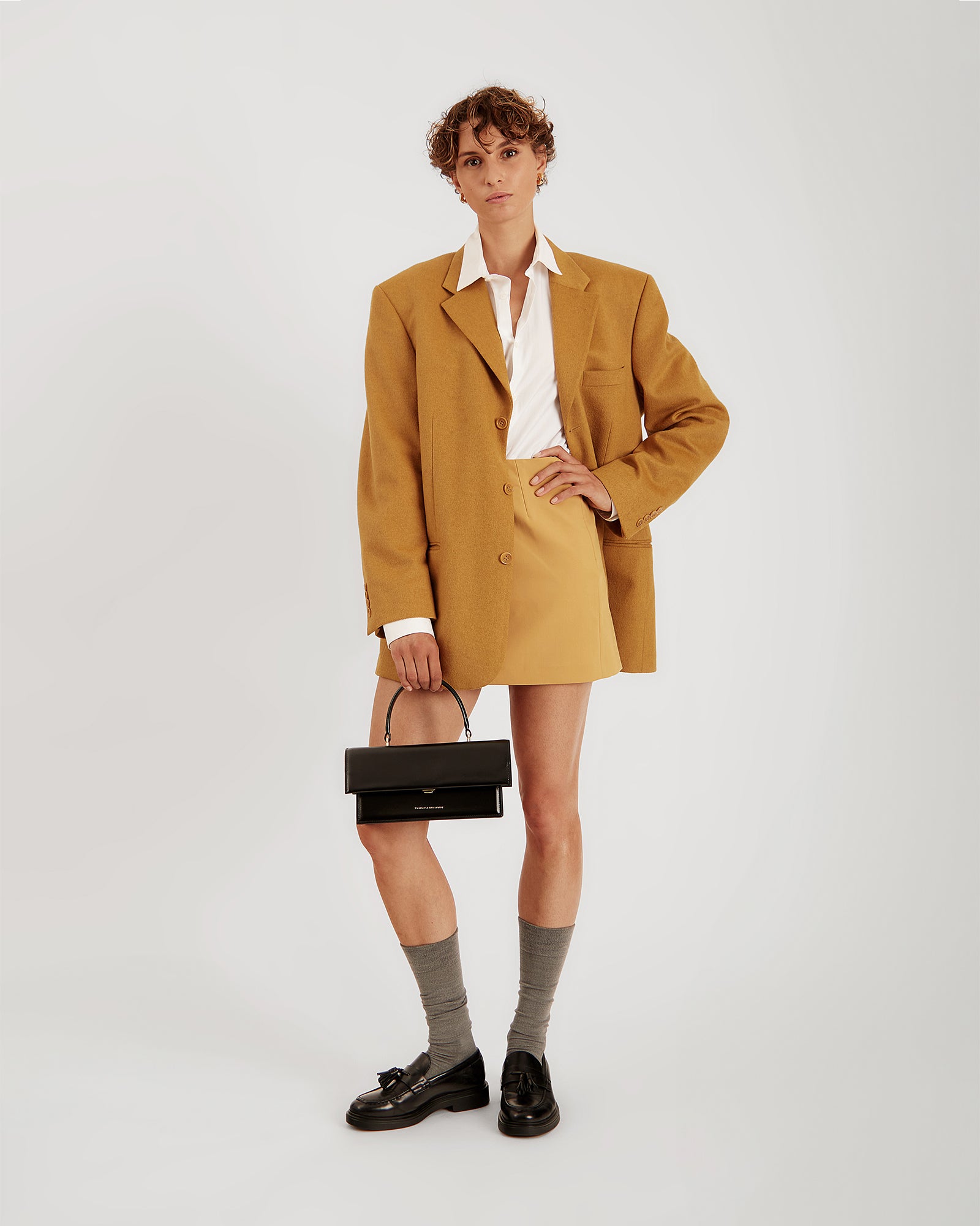 Sac THEA noir porté à la main par anse rigide, tenue oversize jaune moutarde