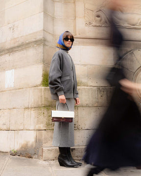 Sac THEA Colourblock art déco porté à la main, vue de profil, rabat oversize, devant une façade en pierre
