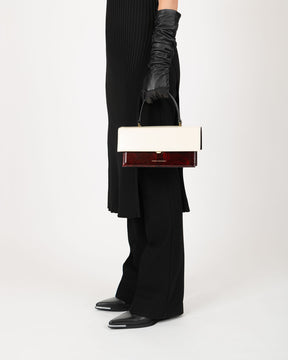 Sac THEA Colourblock art déco porté à la main par sa poignée, vue de profil, coloris écru et rouge bordeaux