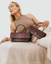 Sac THEA MINI Bordeaux embossé lézard, tenu par la poignée, posé sur canapé