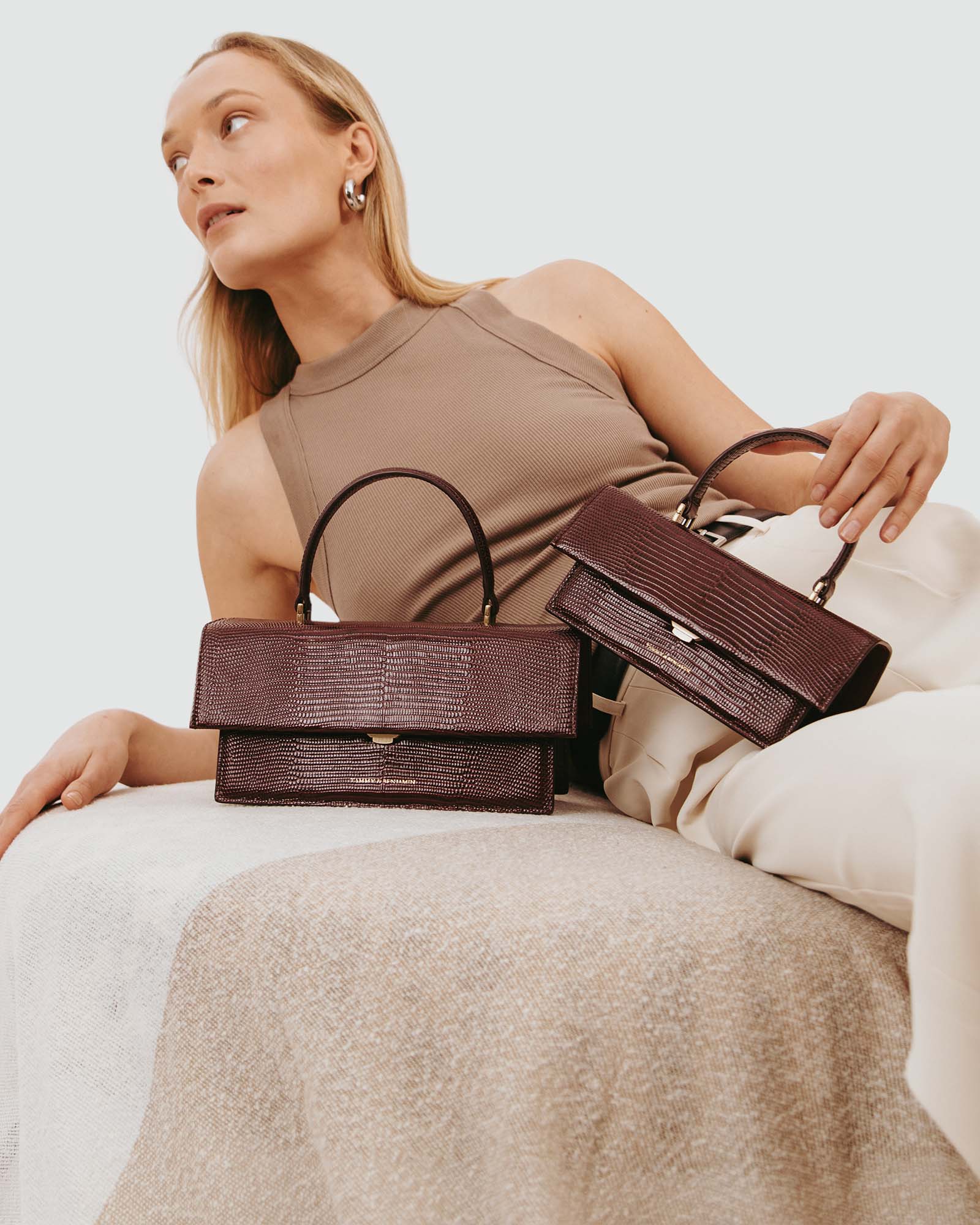 Sac THEA Bordeaux Embossé Lézard tenu par la poignée, posé sur un canapé, porté par le mannequin