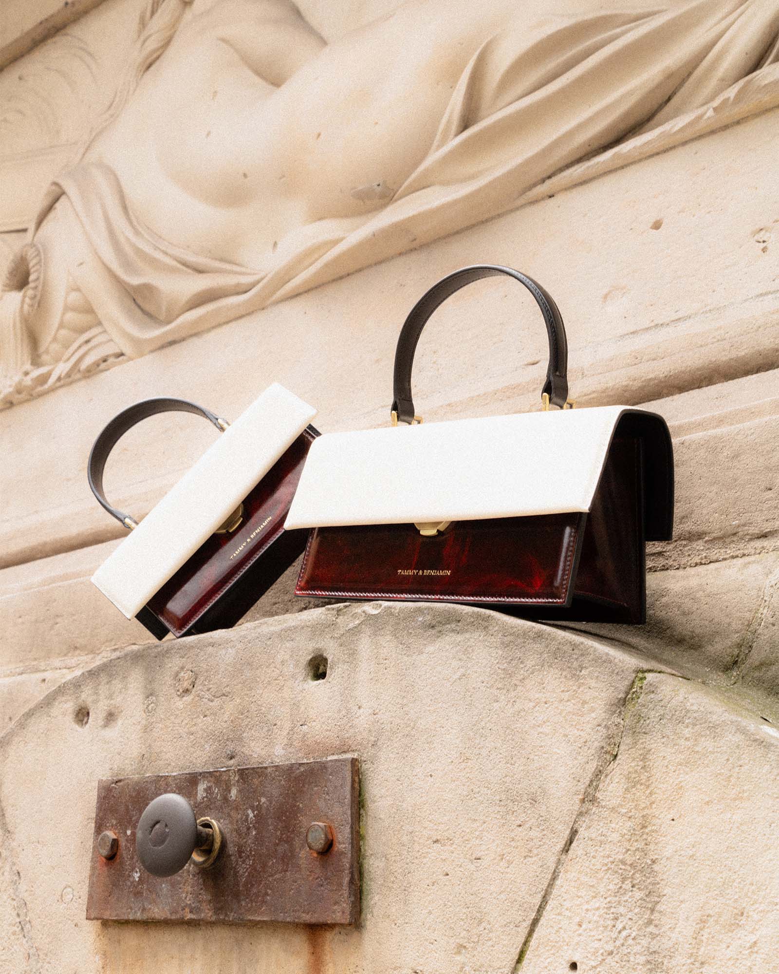 Deux sacs THEA colourblock art déco, rabat ivoire et corps bordeaux, posés sur une pierre sculptée