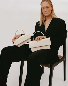 Sac THEA Ivoire tenu à la main par une femme assise, rabat oversize visible, deux sacs portés côte à côte