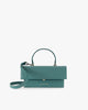 Sac THEA Turquoise de face, rabat fermé, poignée rigide et bandoulière en cuir détachée posée devant