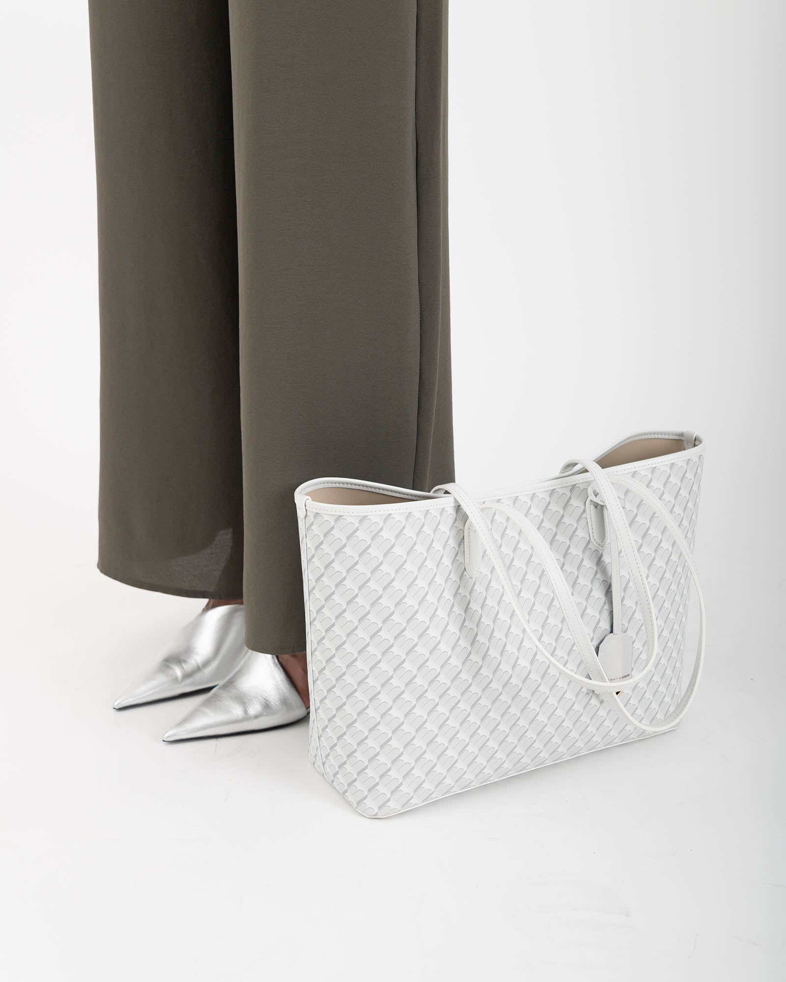 Tote Monogram ivoire posé au sol, vue de profil, anses en cuir tombantes, tenue kaki en arrière-plan