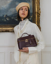 Sac VAYA Aubergine porté à la main, vue de face avec breloque Key Bell et pampille logo