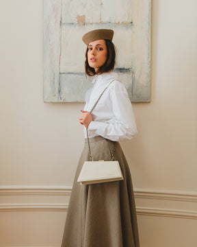 Sac JAY Ivoire porté en bandoulière avec chaîne, vue de côté sur tenue chemise blanche et jupe