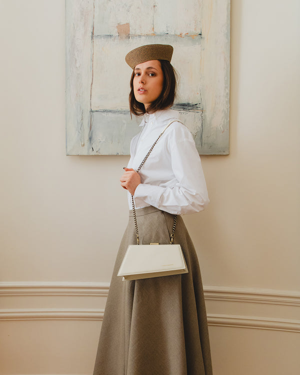 Sac JAY Ivoire porté en bandoulière avec chaîne, vue de côté sur tenue chemise blanche et jupe