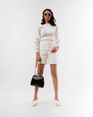 EMMA bag in black naplak, carried by hand, front view, model in white outfit