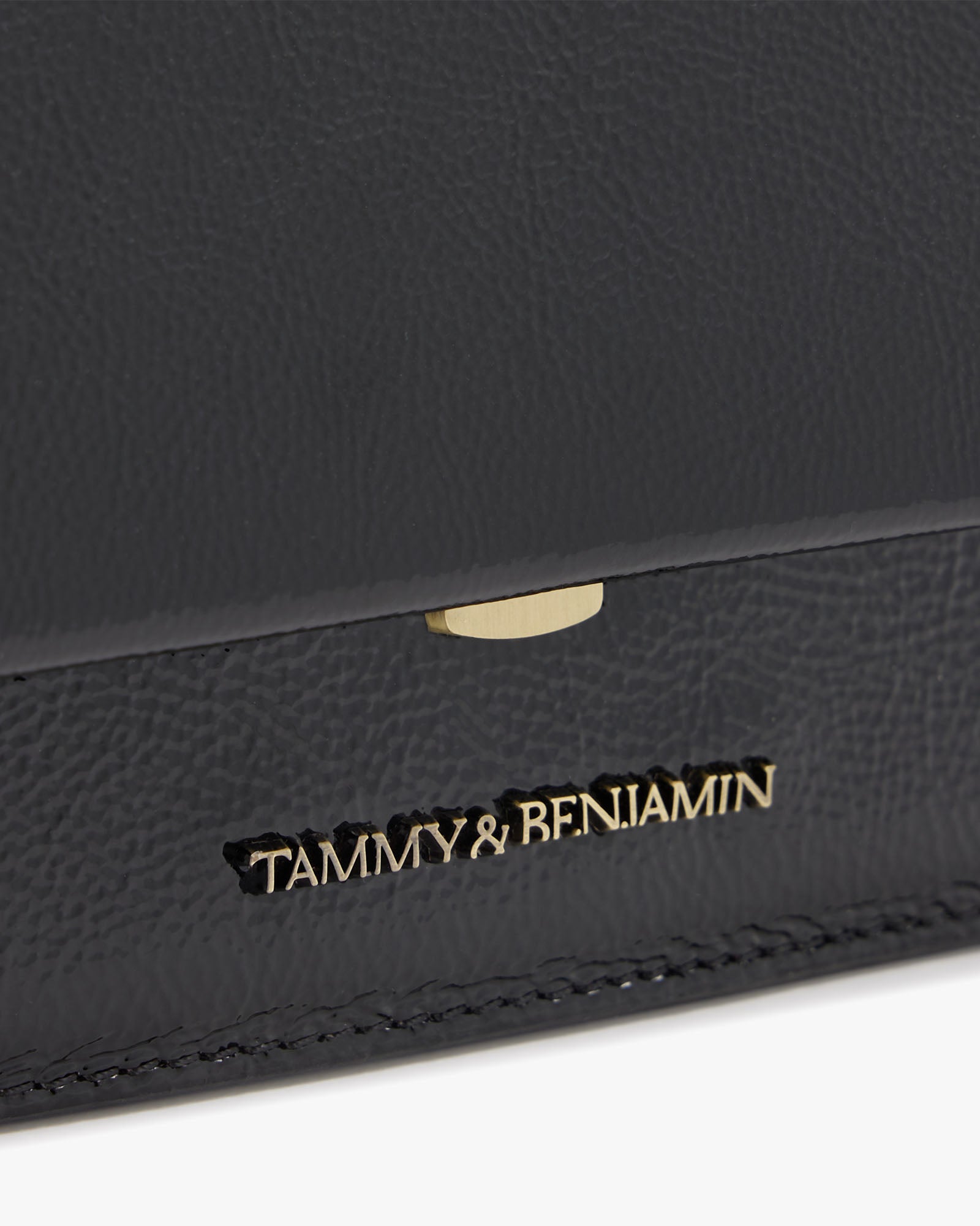 THEA MINI bag in black naplak, close-up of the gold clasp and engraved logo on the flap