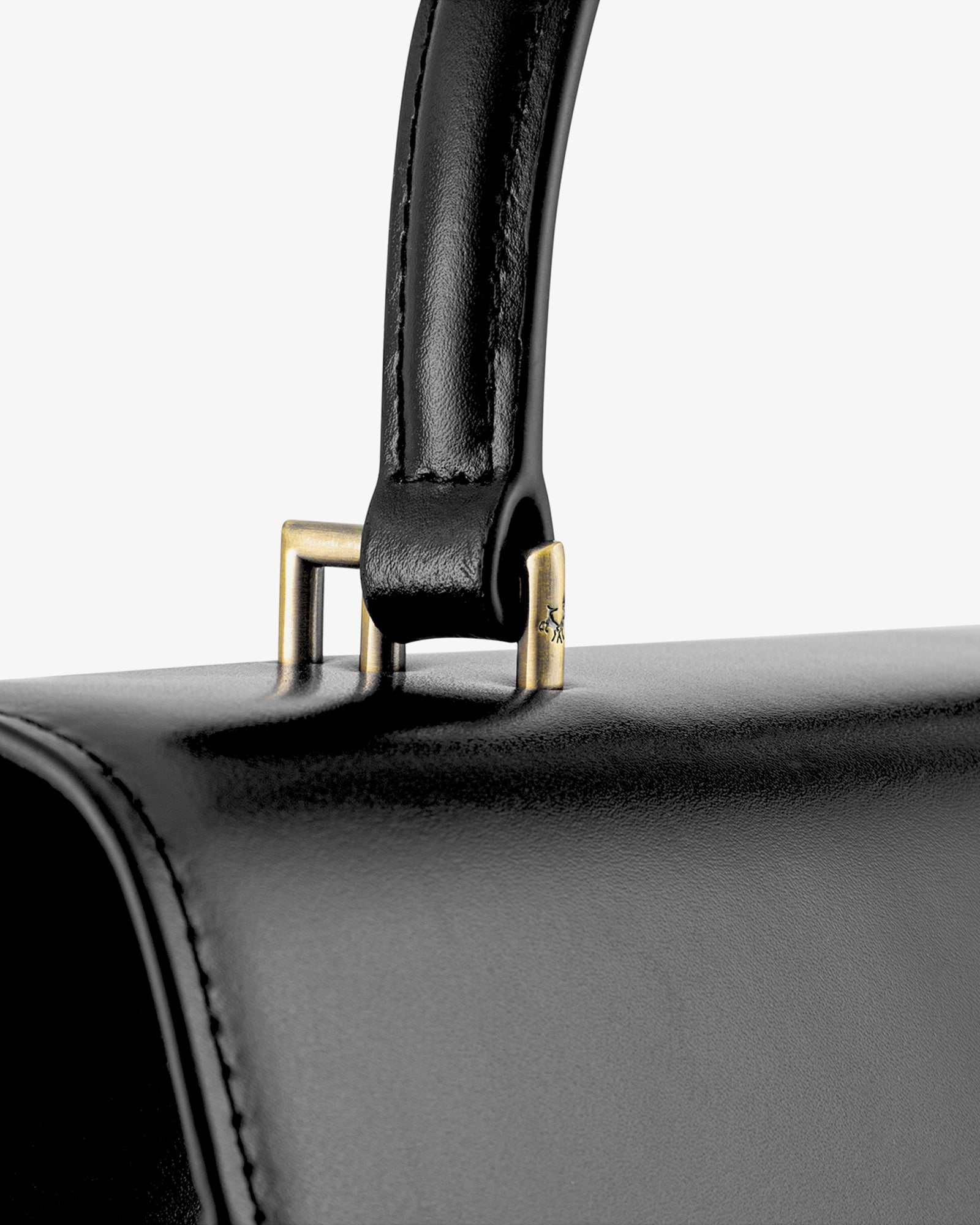 Sac THEA noir en cuir, détail de l'attache métallique dorée entre la poignée rigide et le rabat