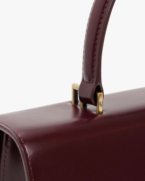 Sac THEA Mahogany, détail de la poignée rigide et des fixations en métal doré