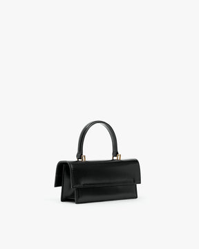 Sac THEA MINI noir, vue de trois quarts arrière, posé, anse courte rigide et rabat oversize visibles
