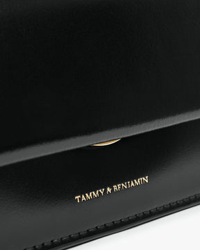 Sac THEA MINI noir, gros plan sur le rabat et le logo doré Tammy & Benjamin